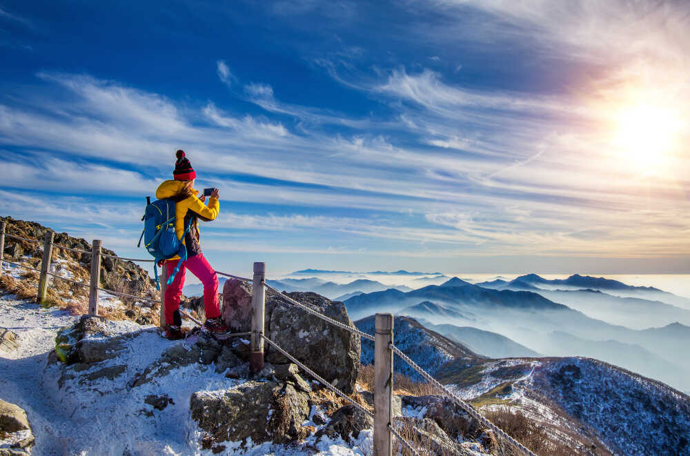 young-woman-hiker-taking-photo-with-smartphone-mountains-peak-winter